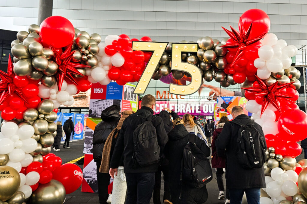 Besucher betreten die Spielwarenmesse Nürnberg durch einen Ballonbogen mit großer Zahl 75 im Eingangsbereich