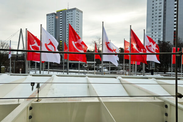 Rote und weiße Flaggen vor dem Messegelände der Spielwarenmesse Nürnberg mit Hochhäusern im Hintergrund im Winter